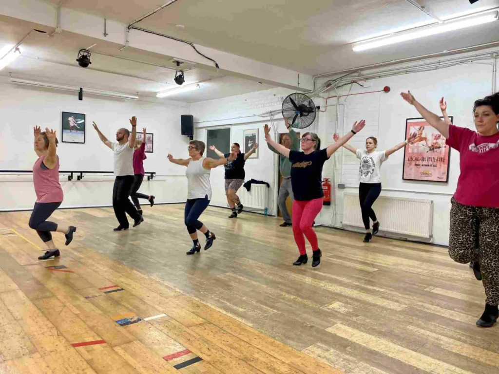 Home 9 Adult beginners in a tap class at Hype Dance's Sheffield studio, with their arms raised and one foot lifted mid-step