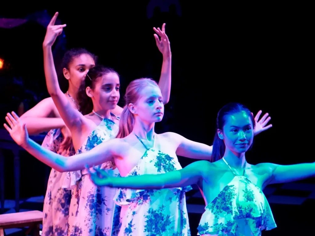 Home 8 Teenage dancers in matching floral dresses performing on stage with their arms raised, at a Hype Dance show